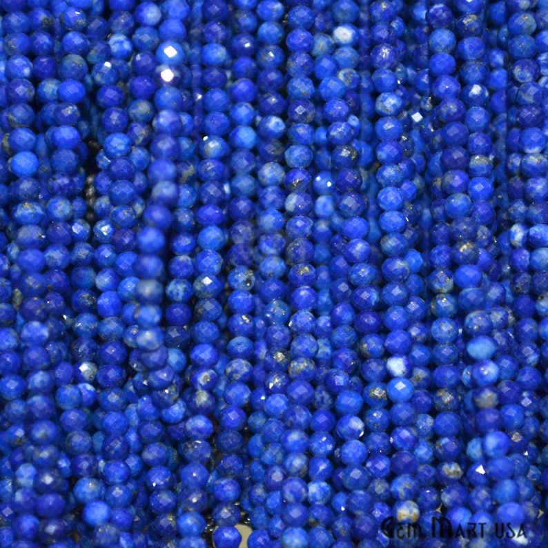 May include: A strand of deep blue lapis lazuli beads, each bead is faceted and has a slightly irregular shape. The beads are strung together on a clear thread.