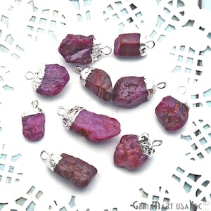 May include: Ten raw ruby gemstone pendants with silver-toned jump rings. The rubies are various shades of pink and red, and some have a rough, natural texture.