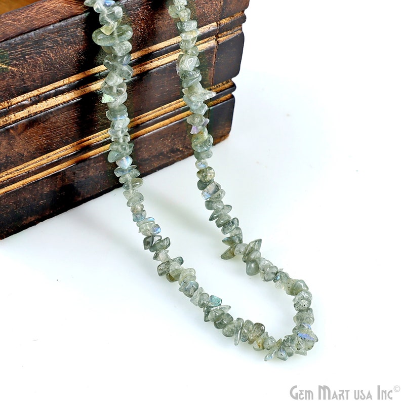 May include: A strand of grey labradorite gemstone chips strung on a cord. The chips are irregular in shape and have a slight iridescent sheen.