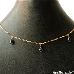 Puede incluir: Un collar de cadena de oro con tres piedras preciosas de amatista colgantes. El collar se muestra sobre un fondo de terciopelo negro.