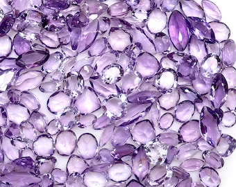 May include: A large collection of loose, faceted amethyst gemstones in various shapes including oval, marquise, round, and pear cuts. The stones display a range of purple hues, from light lavender to deep violet, with reflective surfaces and clear clarity.
