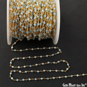 May include: A spool of aquamarine gemstone bead chain with gold-colored wire. The beads are small and round, strung together to create a delicate, shimmering strand. The chain is partially unraveled, showing the intricate detail.
