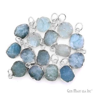 May include: A collection of aquamarine gemstone pendants with silver-colored metal trim and loops. The pendants are various shapes and sizes, with a light blue color and a rough, natural texture. The pendants are displayed on a white background.
