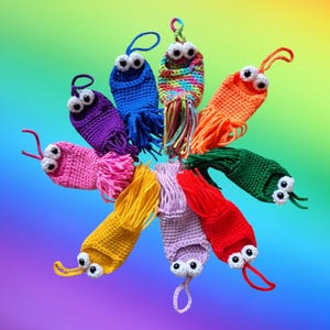May include: A collection of colourful crocheted finger puppets with googly eyes. Each puppet has a long fringe of yarn. The puppets are arranged in a circle, with the fringe extending outwards.