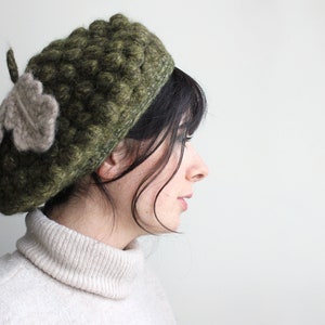 Peut inclure: Béret en crochet vert olive avec un motif en point de bouclette texturé. Il est orné d'une feuille grise claire. Ce chapeau fait main est un accessoire unique et élégant.