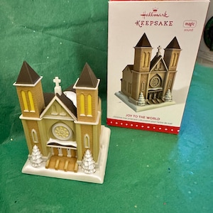 May include: A Hallmark Keepsake Christmas tree ornament shaped like a church. The church is tan with brown accents and a white base. The box reads "JOY TO THE WORLD" and "magic sound".