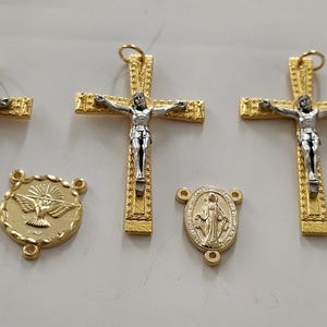Peut inclure: Trois pendentifs crucifix dorés avec des figures argentées de Jésus, deux médailles dorées rondes représentant une colombe et une médaille dorée ovale représentant la Vierge Marie, toutes dotées de petites boucles de fixation.