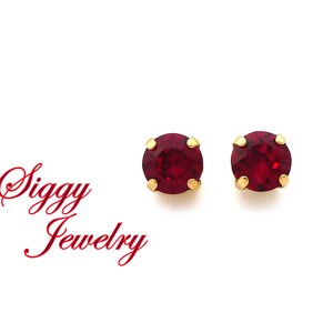 May include: A pair of small, round, red gemstone earrings with gold settings.