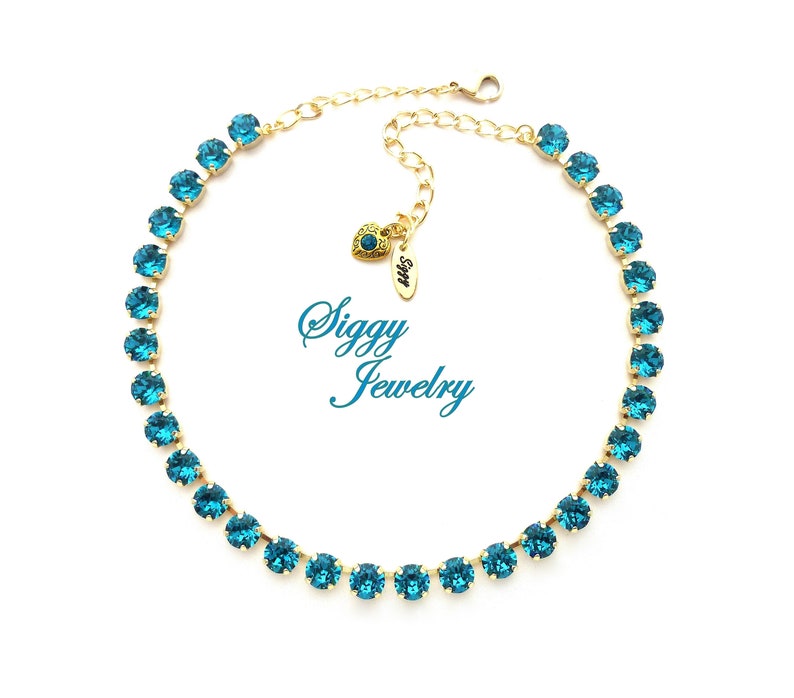 K&ouml;nnte beinhalten: Eine goldene Kettenkette mit einer Reihe von t&uuml;rkisblauen Kristallen. Die Kette hat einen herzf&ouml;rmigen Anh&auml;nger mit dem Text "Siggy Jewelry".