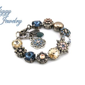 May include: A silver charm bracelet with a variety of colorful crystal charms, including blue, pink, and gold. The charms are in the shape of flowers, stars, and other geometric designs.