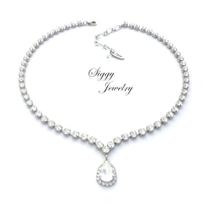 May include: A silver necklace with a teardrop-shaped pendant, both adorned with clear rhinestones. The necklace has a delicate chain and a clasp closure. The pendant is surrounded by a halo of smaller rhinestones. The necklace is labeled "Siggy Jewelry".