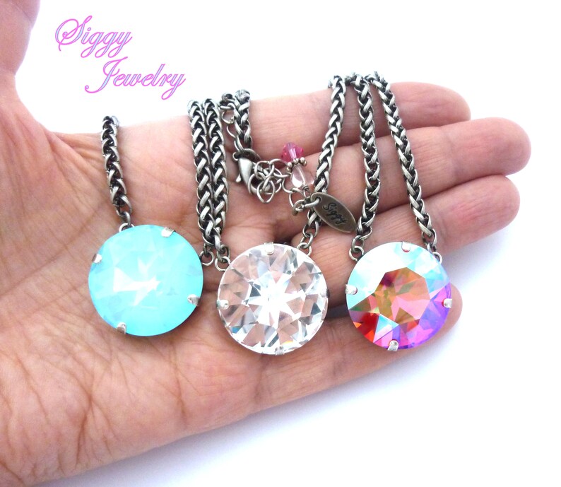 May include: Three silver chain necklaces with round crystal pendants. The pendants are in shades of blue, clear, and pink.