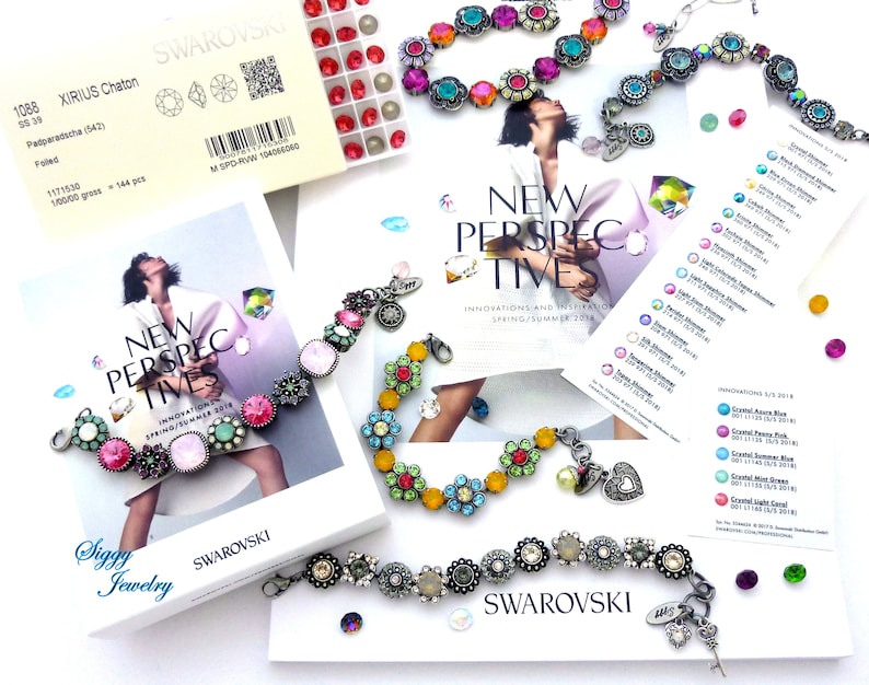 May include: A close-up of three colorful bracelets with flower-shaped charms. The bracelets are made of metal and feature crystals in various colors, including pink, blue, green, and yellow. The bracelets are arranged on a white surface with a brochure for Swarovski crystals.