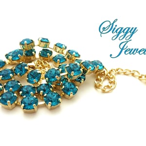 K&ouml;nnte beinhalten: Eine goldene Halskette mit einer Kette aus t&uuml;rkisblauen Kristallen und einem kleinen goldenen Herzanh&auml;nger mit einem t&uuml;rkisblauen Kristall. Die Halskette hat ein Etikett mit der Aufschrift "Siggy Jewelry".