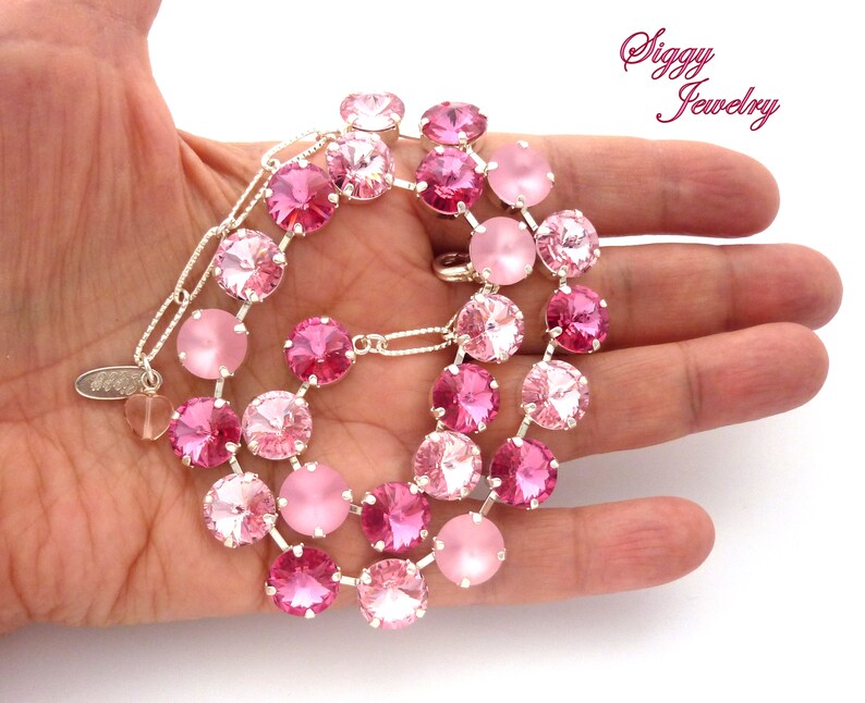 Pode incluir: Um colar de cristal rosa com uma corrente de prata. O colar apresenta um degrad&ecirc; de cristais rosa, com os cristais rosa mais claros na parte superior e os cristais rosa mais escuros na parte inferior. O colar est&aacute; em uma m&atilde;o, e o texto "Siggy Jewelry" &eacute; vis&iacute;vel no fundo.