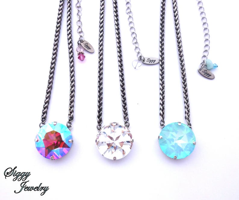 May include: Three silver chain necklaces with different colored crystal pendants. The pendants are round and have a faceted design. The necklaces are on a white background.