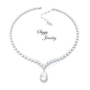 May include: A silver necklace with a teardrop-shaped pendant set with clear rhinestones. The necklace is made of small, clear rhinestones that are set in a silver chain. The pendant is also set with clear rhinestones and has a halo of smaller rhinestones around it. The necklace is labeled "Siggy Jewelry".