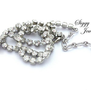 May include: A silver necklace with a teardrop-shaped crystal pendant and a chain of small crystals. The necklace has a silver clasp and a small tag with the word "Siggy" on it.
