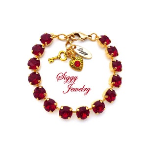 Pode incluir: Uma pulseira dourada com pedras preciosas vermelhas vibrantes. A pulseira inclui um berloque com uma chave, um coração e uma etiqueta que diz "Siggy". O texto "Siggy Jewelry" também é visível.