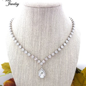 May include: A silver necklace with a teardrop-shaped pendant set with clear rhinestones. The necklace is on a white fabric-covered mannequin.