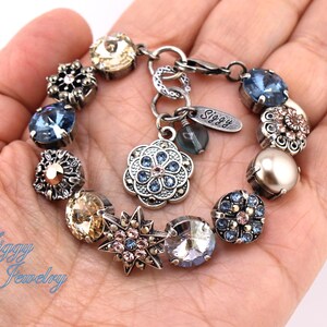 May include: A silver charm bracelet with a variety of blue, gold, and pink charms. The charms include flowers, stars, and crystals. The bracelet has a silver clasp and a tag that says "Siggy".