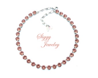 May include: A silver chain necklace with a row of light pink crystal stones. The necklace is on a white background. Siggy Jewelry.