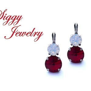 May include: A pair of silver earrings with a red and white crystal design. The earrings feature a larger red crystal and a smaller white crystal.