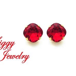 Könnte beinhalten: Ein Paar rote Edelsteinohrringe mit goldenen Fassungen. Die Ohrringe sind quadratisch und haben ein facettierten Design. Die Ohrringe sind vor einem weißen Hintergrund platziert.