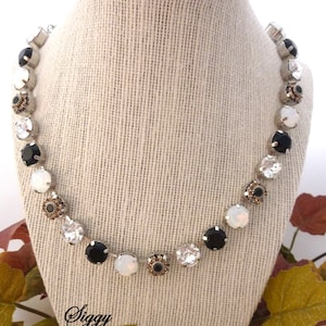 May include: A silver-toned necklace with alternating black, white, and clear round gemstones. Some gemstones have a bronze-colored center. The necklace is displayed on a mannequin. The text "Siggy Jewelry" is visible.