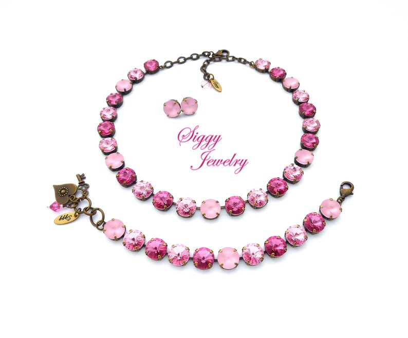 Pode incluir: Um conjunto de colar e pulseira rosa e ouro rosa com um fecho em forma de cora&ccedil;&atilde;o. O conjunto apresenta um degrad&ecirc; de cristais rosa.