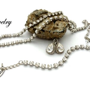 May include: A silver necklace with a teardrop-shaped pendant, a matching bracelet, and a pair of teardrop-shaped earrings. All pieces are adorned with clear rhinestones.