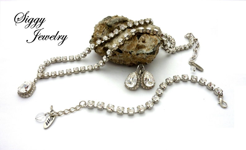 May include: A silver necklace with a teardrop-shaped pendant, a matching bracelet, and a pair of teardrop-shaped earrings. All pieces are adorned with clear rhinestones.
