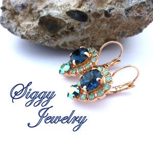 Pu&ograve; includere: Un paio di orecchini pendenti con un cristallo blu a forma di lacrima circondato da cristalli pi&ugrave; piccoli di colore blu chiaro. Gli orecchini sono in metallo dorato rosa e hanno una chiusura a gancio.