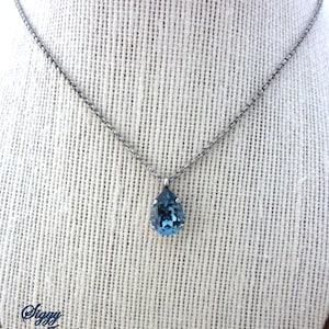 Op de afbeelding: Een zilveren ketting met een traanvormige blauwe kristallen hanger.
