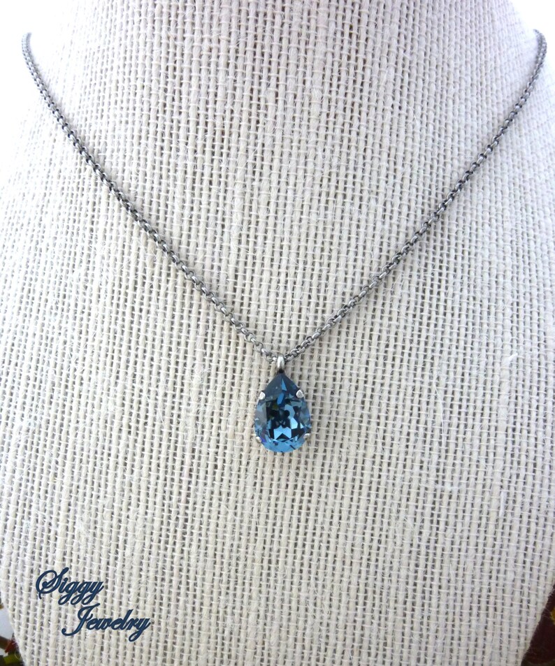 Op de afbeelding: Een zilveren ketting met een traanvormige blauwe kristallen hanger.