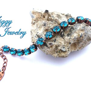 K&ouml;nnte beinhalten: Ein Kupferarmband mit t&uuml;rkisblauen Kristallen. Das Armband liegt auf einem Stein mit dem Schriftzug "Siggy Jewelry" im Hintergrund.