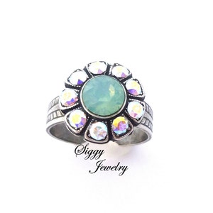 May include: A silver ring with a green opal stone surrounded by clear iridescent crystals in a flower shape.