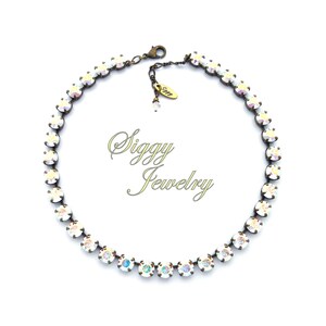 May include: A delicate, iridescent white crystal necklace with an antique brass chain and clasp. The necklace is made of small, round crystals that are set close together. The necklace is approximately 16 inches long and has a 2-inch extender chain.