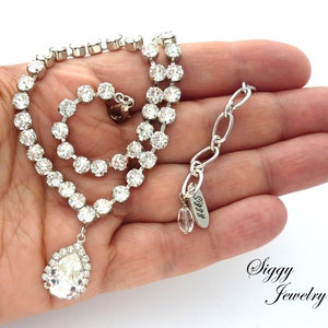May include: A silver necklace with a teardrop-shaped crystal pendant and a chain of small round crystals. The necklace has a silver clasp and a small tag that says "Siggy".