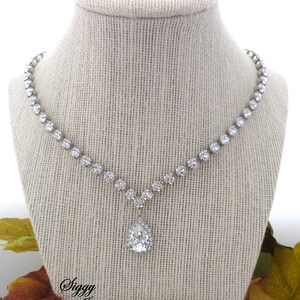 May include: A silver necklace with a teardrop-shaped pendant, both adorned with clear rhinestones. The necklace is displayed on a fabric-covered mannequin.