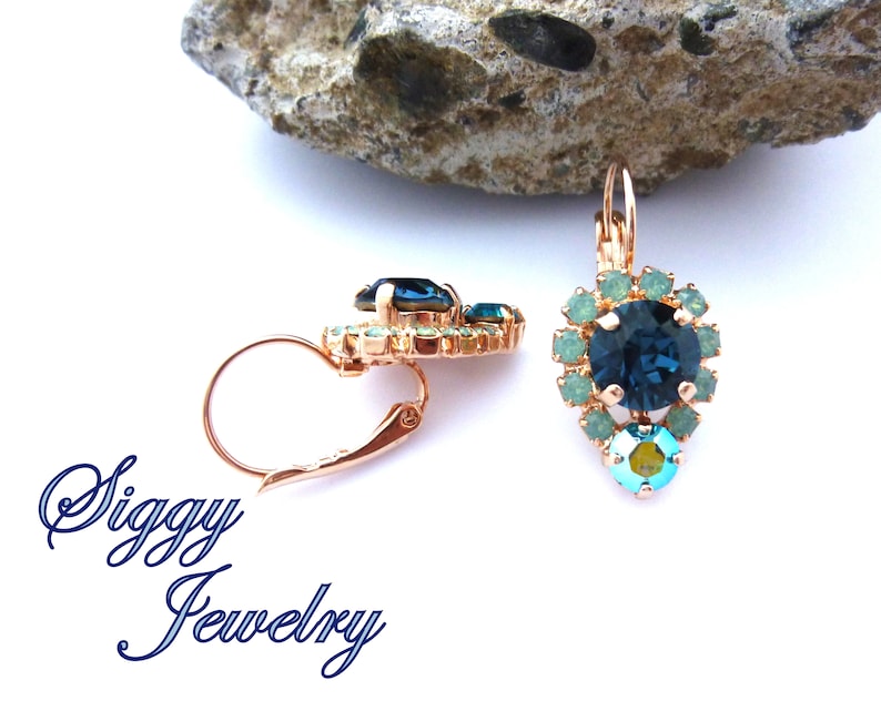 Pu&ograve; includere: Orecchini pendenti in oro rosa con un grande cristallo blu circondato da cristalli turchesi pi&ugrave; piccoli. Gli orecchini hanno una chiusura a leva.
