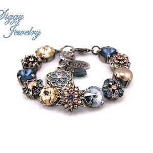 May include: A silver charm bracelet with a variety of blue, pink, and gold crystal charms. The charms include flowers, stars, and a round charm with a floral design. The bracelet has a silver clasp and a small tag that says "Siggy".