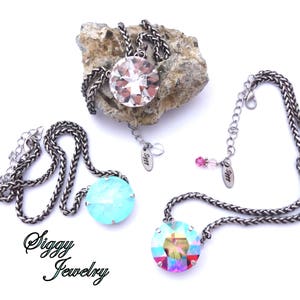 May include: Two silver chain necklaces with large crystal pendants. One pendant is clear and the other is turquoise. Both necklaces have a small tag with the text "Siggy Jewelry".