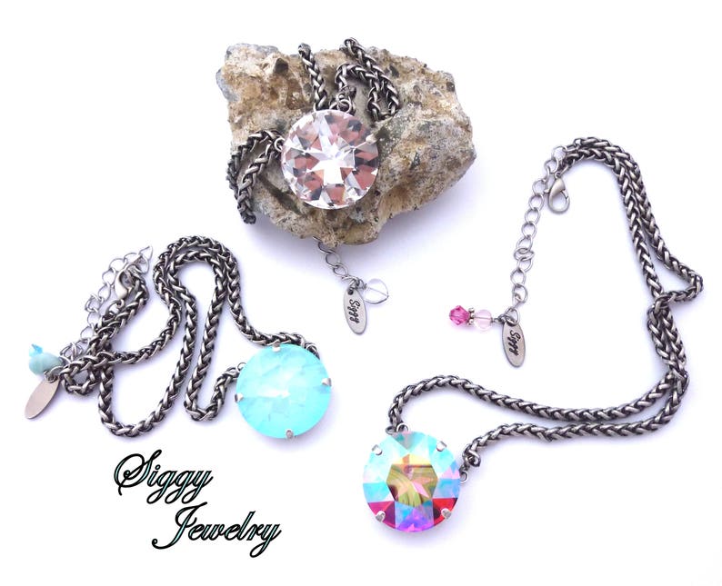 May include: Two silver chain necklaces with large crystal pendants. One pendant is clear and the other is turquoise. Both necklaces have a small tag with the text "Siggy Jewelry".
