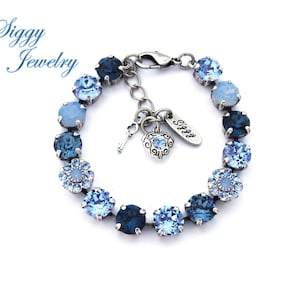 May include: A blue crystal bracelet with a silver clasp and charm. The bracelet features a gradient of blue crystals, from light blue to dark blue. The charm is a silver key and heart with a blue crystal.