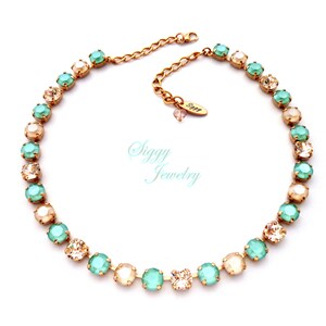Pode incluir: Um colar de corrente dourada com contas de cristal alternadas de cor verde claro e creme. O colar tem uma pequena etiqueta com a palavra "Siggy Jewelry".