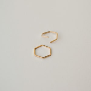 May include: Two gold hexagonal hoop earrings. The earrings are simple and minimalist in design.