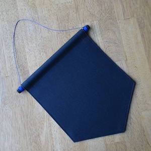 May include: A dark blue fabric pennant with a rolled top and a blue string attached. The pennant is hanging on a wooden surface.