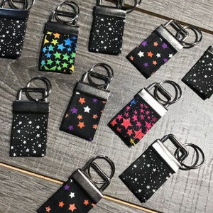 May include: Assortment of keychains with different star patterns. The keychains are made of fabric and have a silver metal ring. The patterns include black and white stars, colorful stars, and pink and white stars.