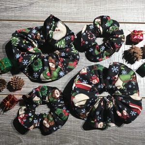 May include: Set of four black scrunchies with a snowman and Christmas-themed print. The scrunchies are made of fabric and have a gathered design.